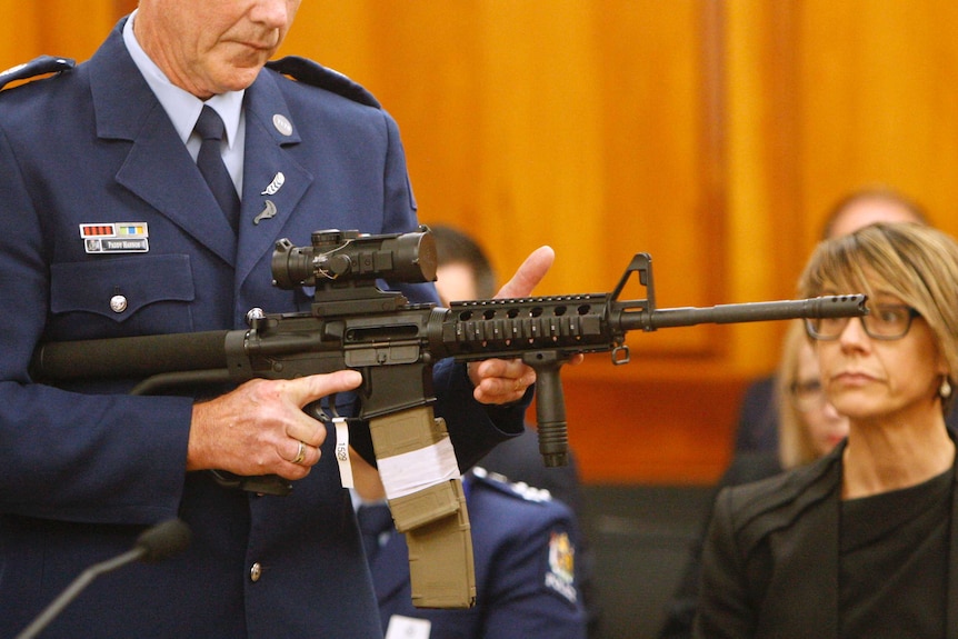 A New Zealand police officer holds an assault rifle in front of parliamentarians.