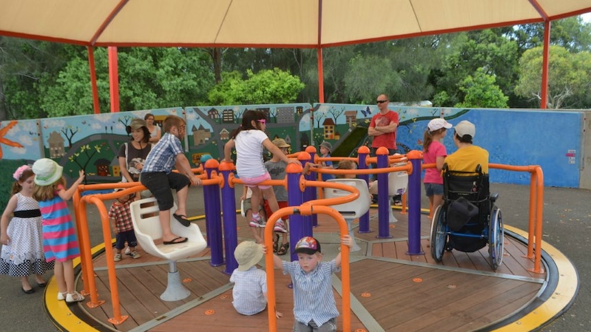 A playground carousel with children of different ages, someone in a wheelchair.