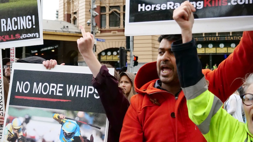 Protesters with fists in the air outside Flinders Street Station hold signs saying no more whips and horse racing kills.