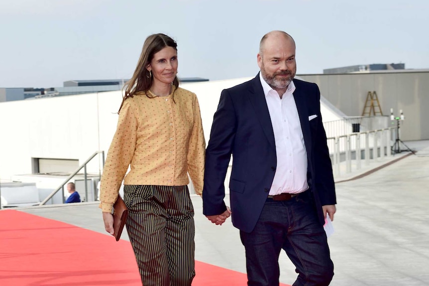 A man and woman hold hands and walk on a red carpet.