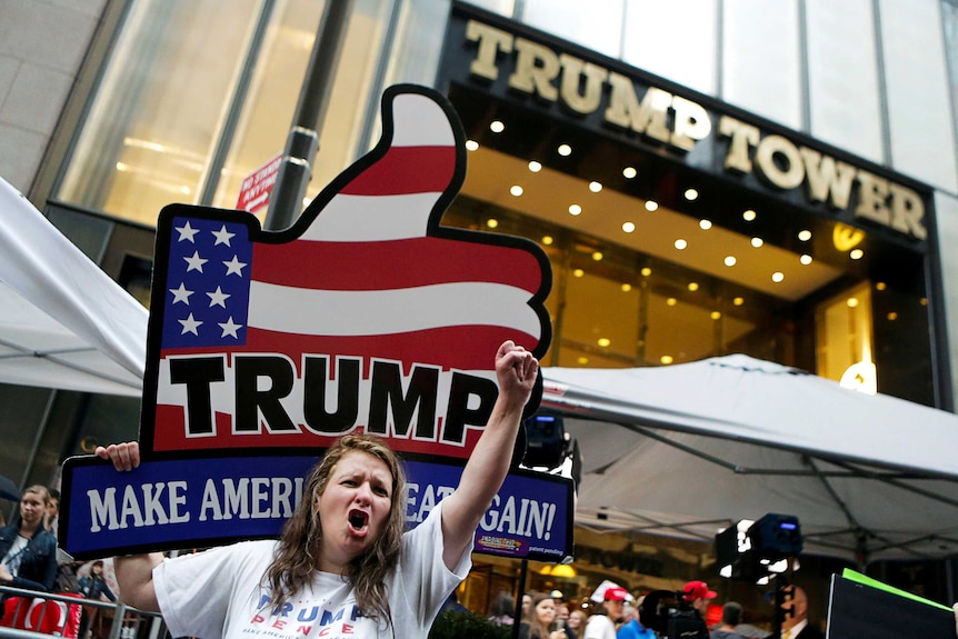A supporter raises her fist and displays a trump "make america great again" sign outside trump tower.