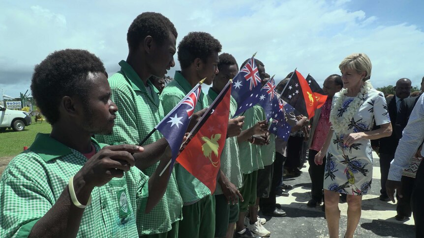 Wide shot of a line of boys holding flags as a woman walks beside them.