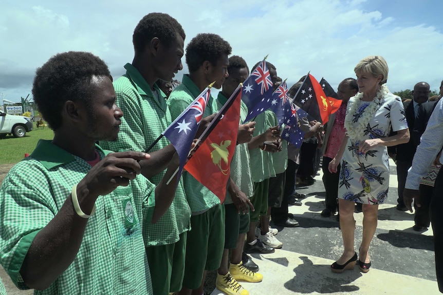 Wide shot of a line of boys holding flags as a woman walks beside them.