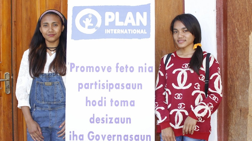 Odelia, 18, and Elfia, 19, stand next to a PLAN International.