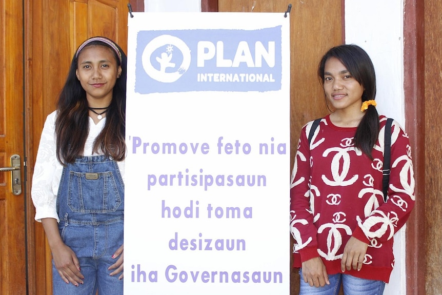 Odelia, 18, and Elfia, 19, stand next to a PLAN International.