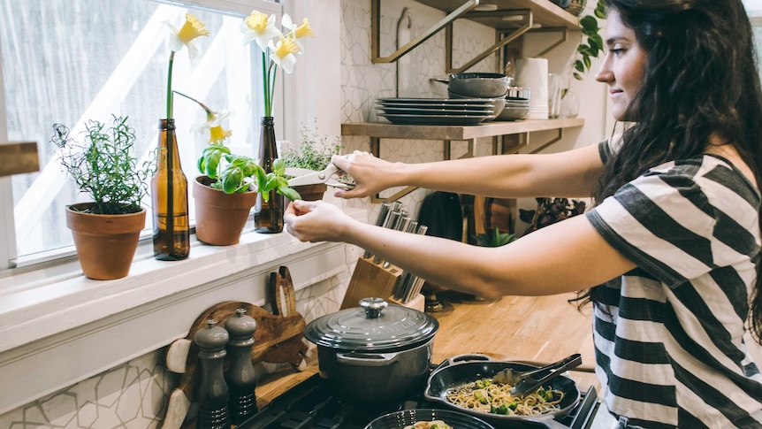 A woman cuts fresh basil leaves from her windowsill, to garnish a dinner made for one during coronavirus.