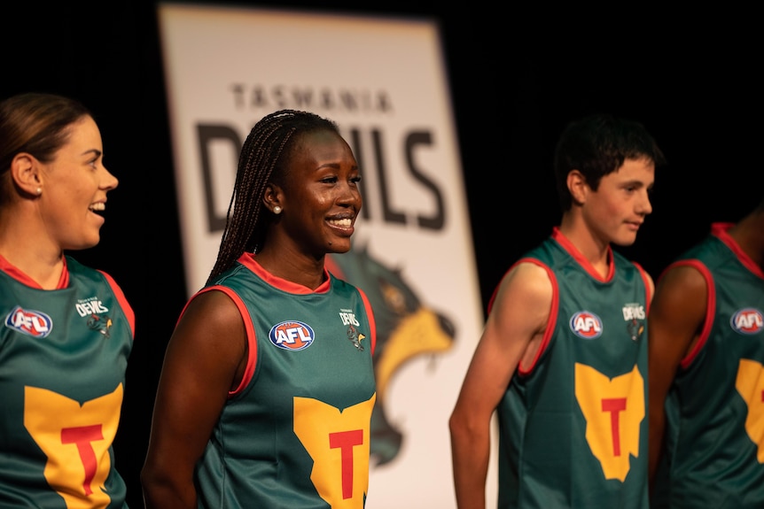 Three people wear football guernseys on a stage.