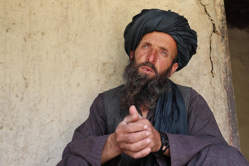 A man with a beard and wearing a head coverings wears a serious expression as he is interviewed.