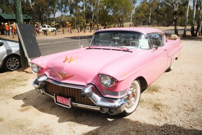 A pink Cadillac parked outside on dirt verge