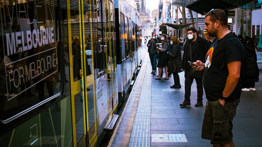 Passengers wait on a platform to board a Melbourne tram.