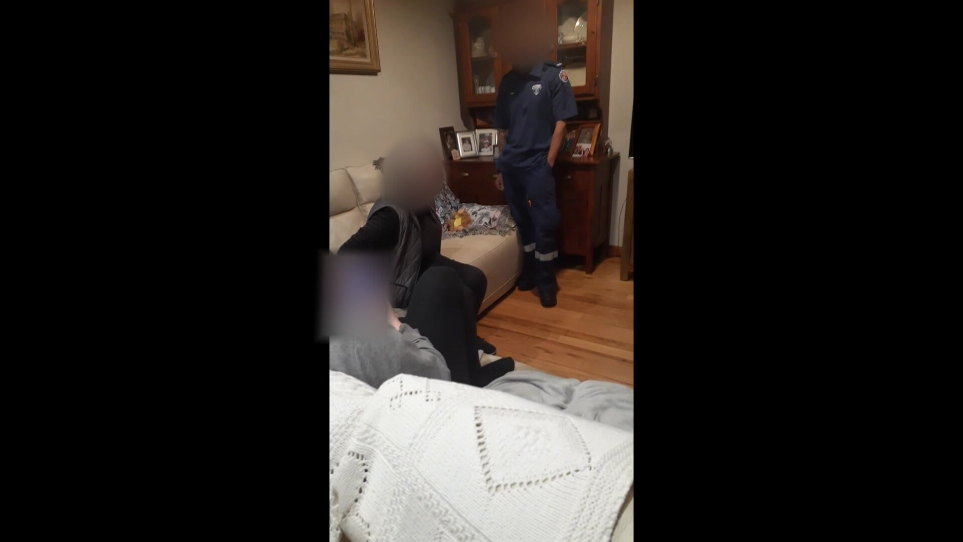 A woman and paramedics in a living room, with faces blurred.