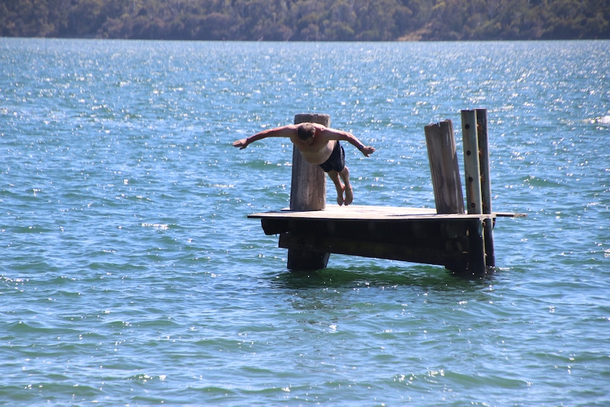A man dives off of a free standing diving board out at sea.