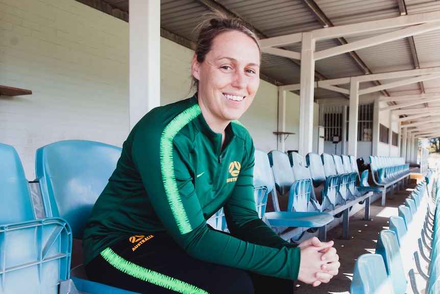 A woman wearing green and black sits in a grandstand