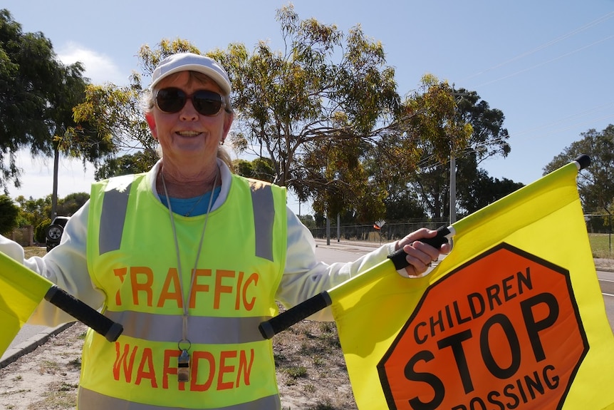 Lollipop lady, wearing high-viz vest, stands with her flags