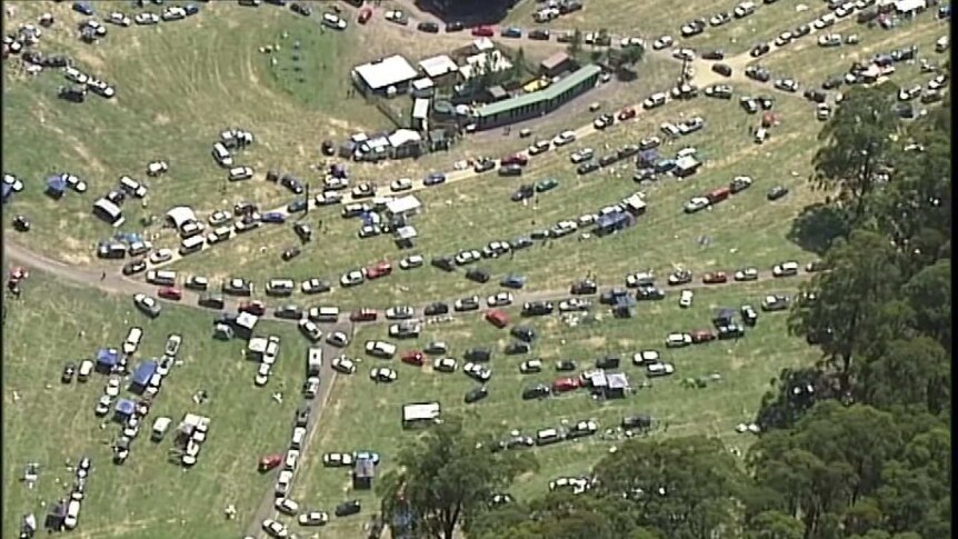 An aerial shot of hundreds of cars on grass, driving out of a music festival venue.