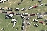 An aerial shot of hundreds of cars on grass, driving out of a music festival venue.