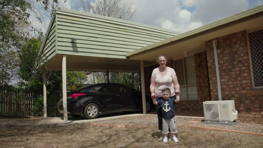 Laura Christopher holding her son on her hip, standing in front of her house