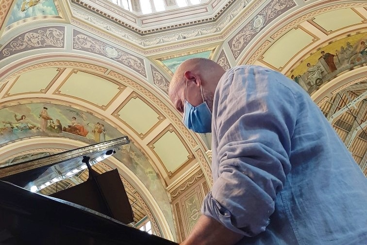 A low angle photo of a man playing piano with the Melbourne Exhibition Centre roof in the background.