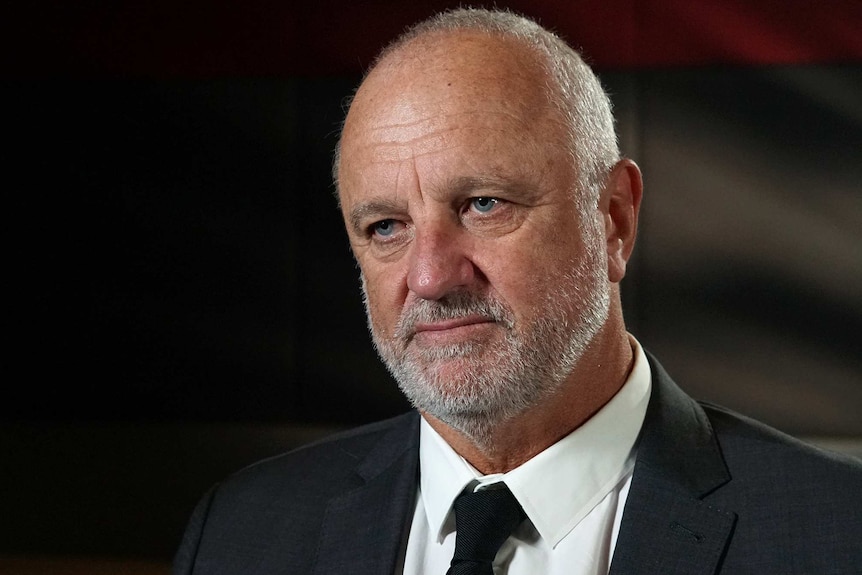 A head and shoulders shot of Graham Arnold looking serious during an indoors interview while searing a suit and tie.