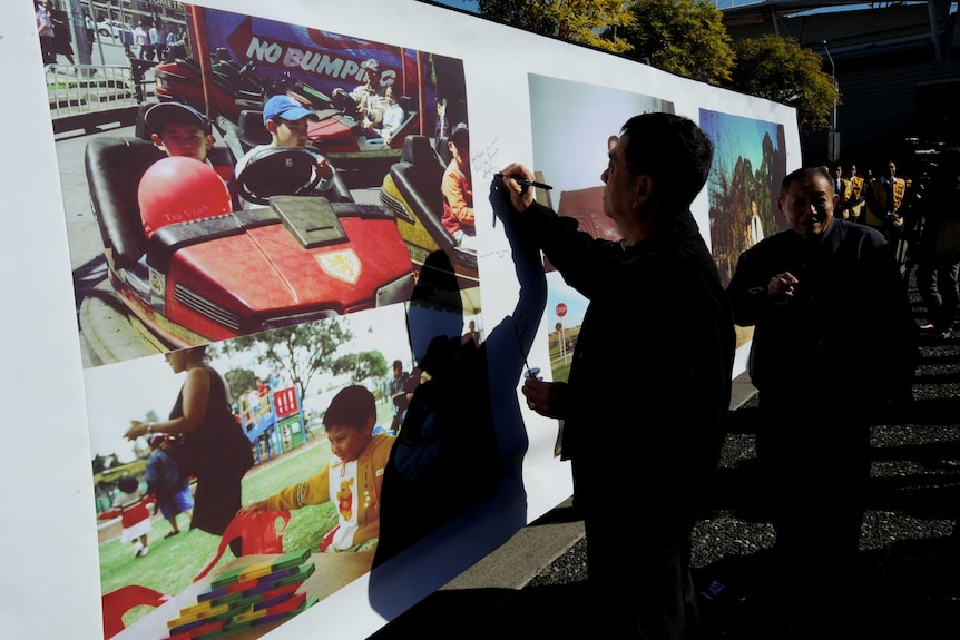 A man signs a big photo of the Lin family.