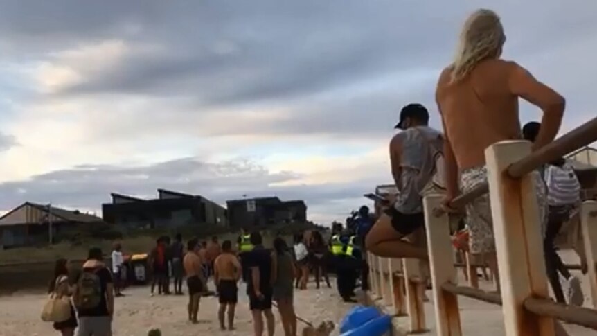 Police officers in fluro yellow vests stand amongst people at the beach at Chelsea.