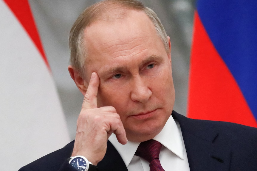 Vladimir Putin rests his head against his hand, with one finger pointed towards his temple