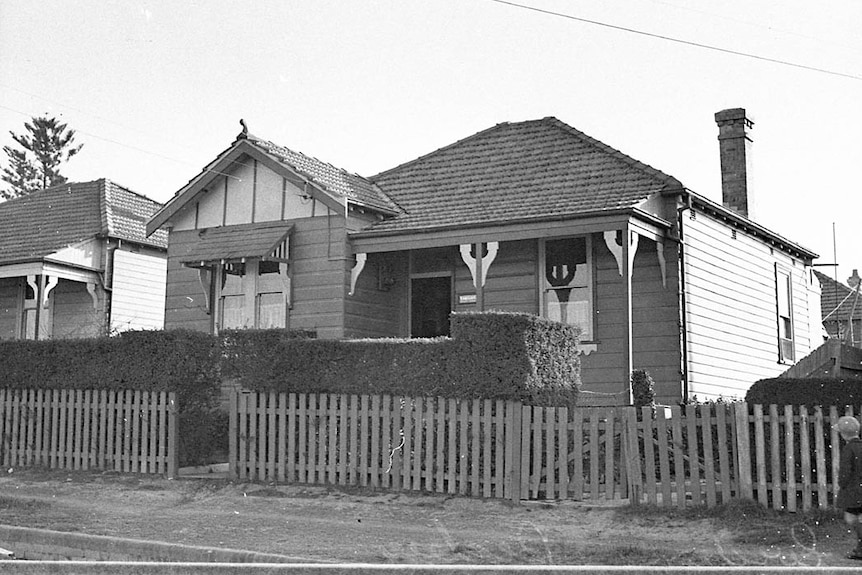 A black and white photo of a weatherboard house with a picket fence taken in 1935