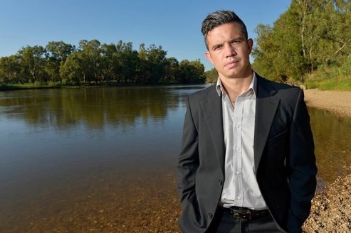 An Indigenous man dressed in a suit stands next to a river in a regional location