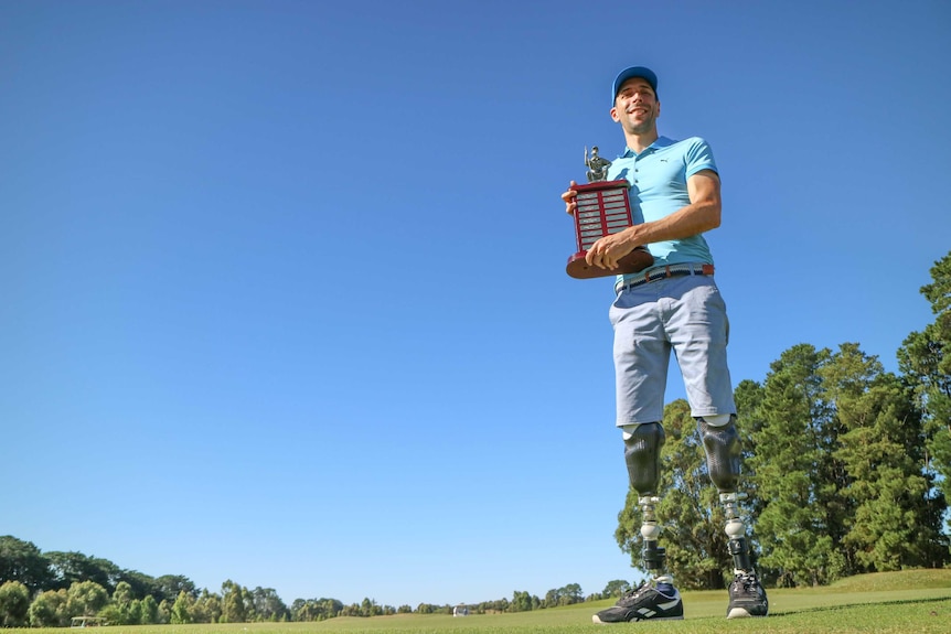 Upward shot of Mike Rolls holding 2018 Victorian Amputee Open trophy