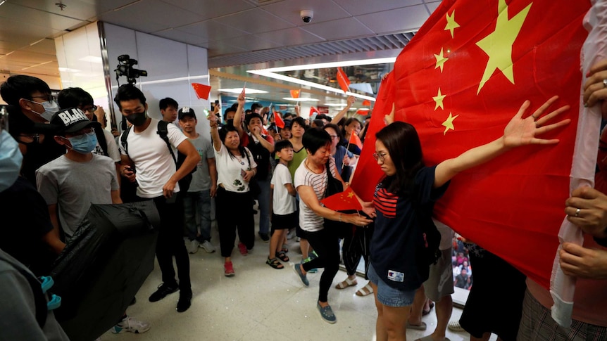 Pro-Hong Kong and pro-China protesters stand opposite each other as one woman spreads her arms over a large Chinese flag.