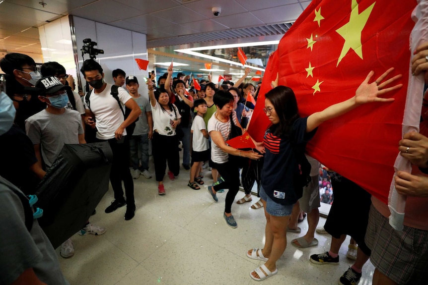 Pro-Hong Kong and pro-China protesters stand opposite each other as one woman spreads her arms over a large Chinese flag.