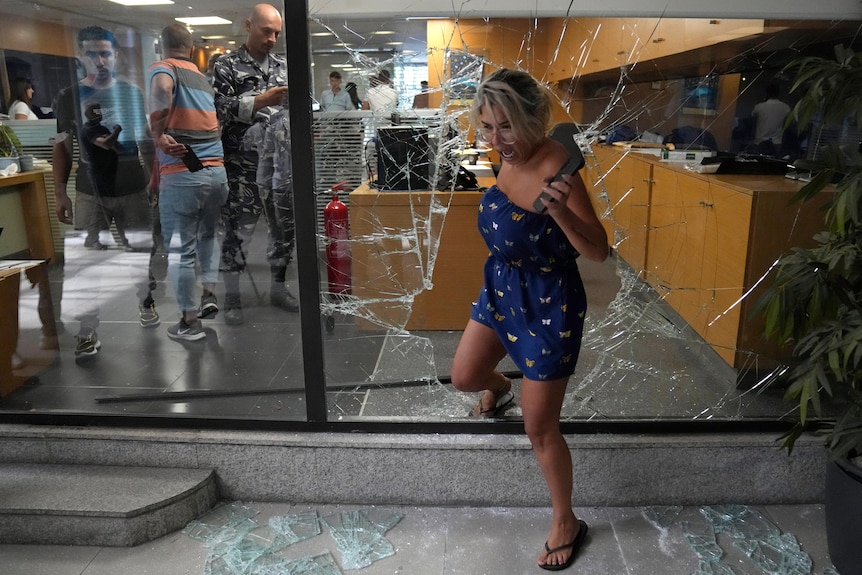 A bank employee screams as she exits the bank through a window broken by attackers.