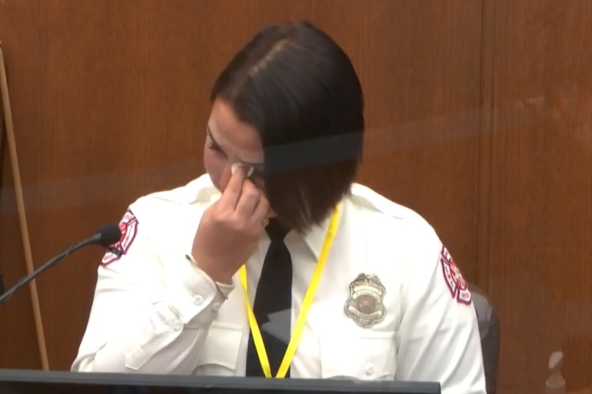 A woman in court wearing her uniform wiping her eyes.