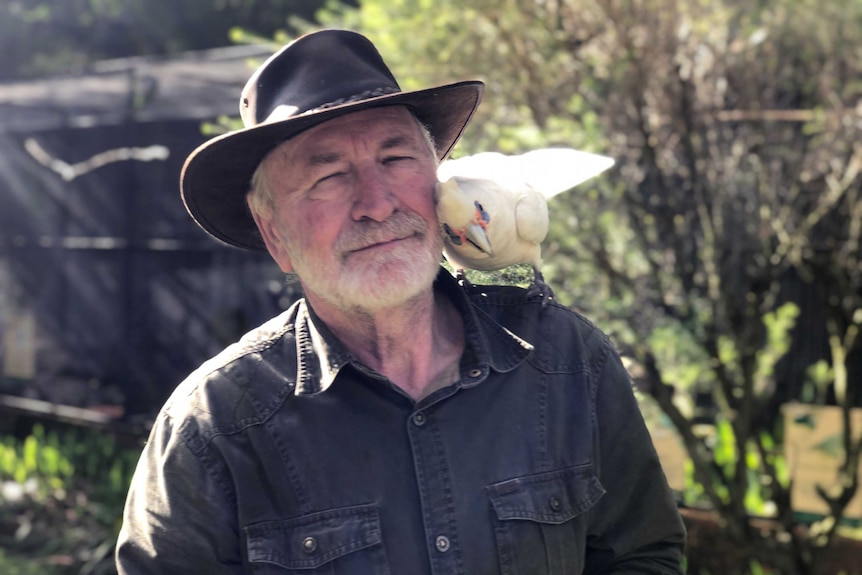 A man in an akubra with a cockatoo on his shoulder.