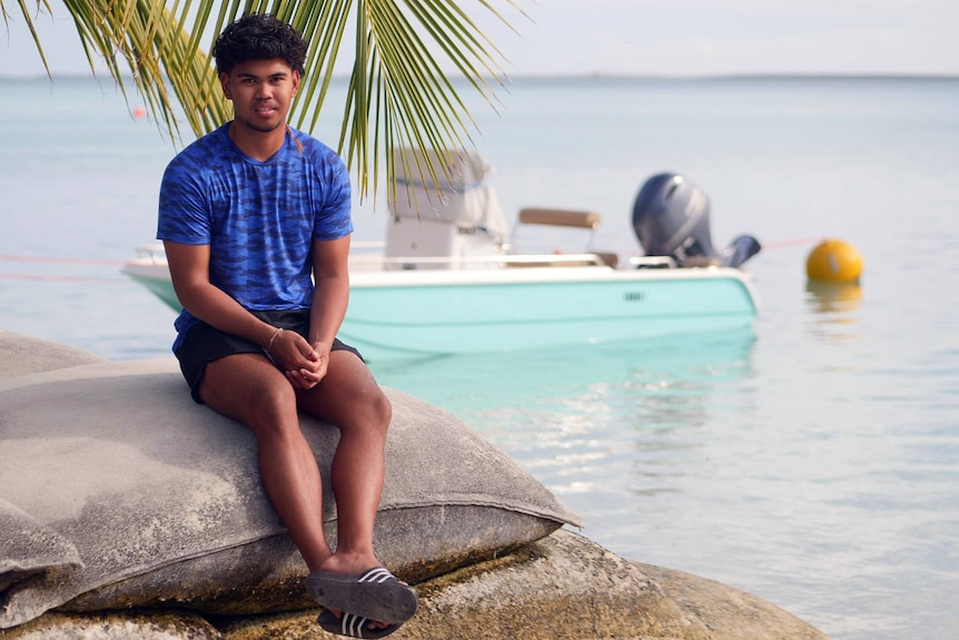 Cocos Island high school student Izaiah sits by the water on the protective sand-bag sea wall at Home Island. 