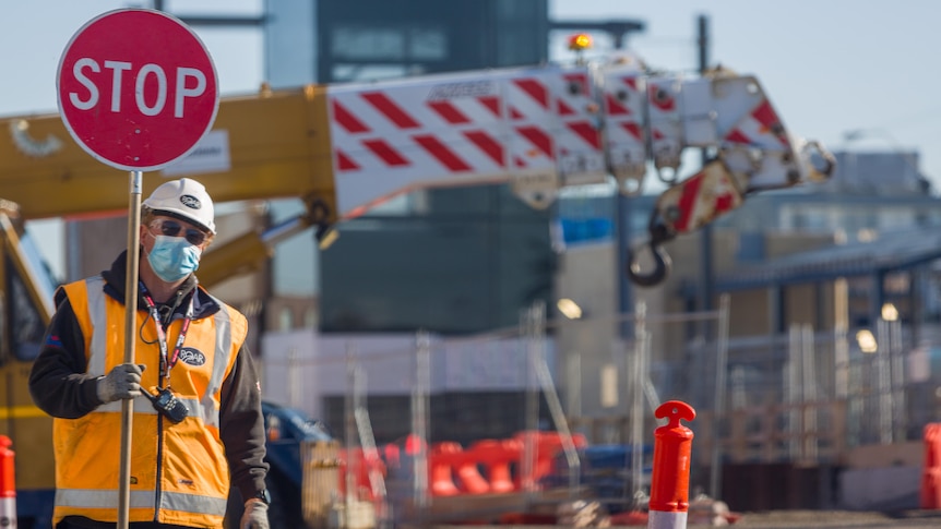 A man wearing high-vis clothing holds a sign at a construction site.