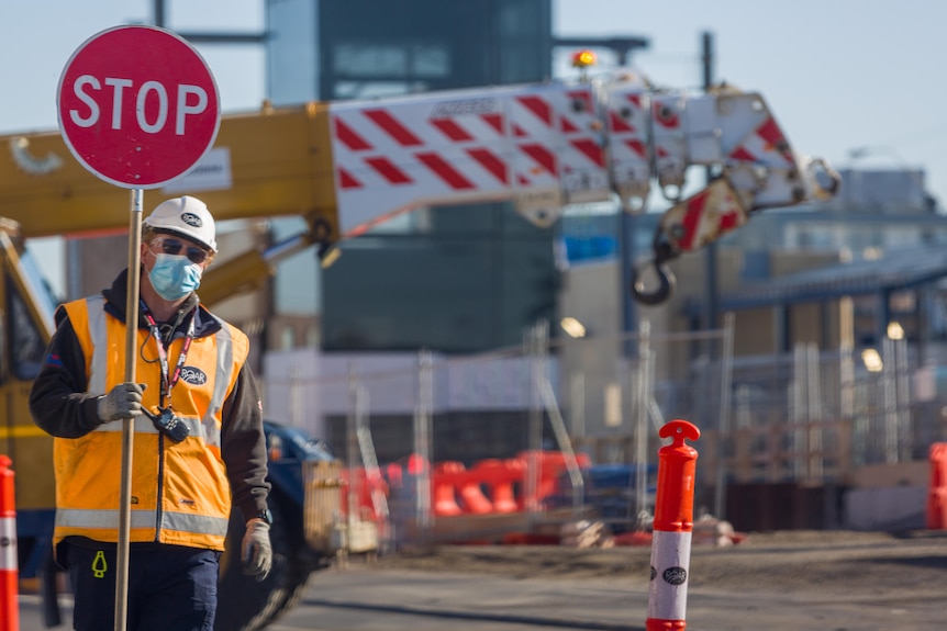 A man wearing high-vis clothing holds a sign at a construction site.