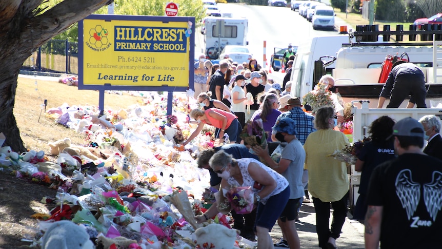People collecting flowers and teddy bears outside a primary school.
