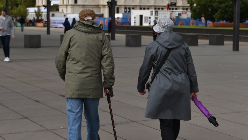 An elderly couple is seen in Melbourne, with a walking stick and umbrealla.