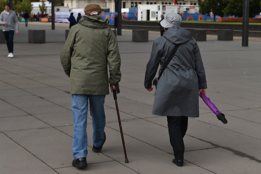 An elderly couple is seen in Melbourne, with a walking stick and umbrealla.