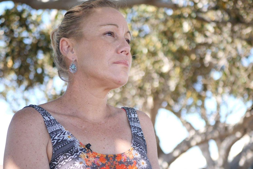 Renee Bell, woman, looks out into the distance. She wears a colourful singlet and is surrounded by trees.