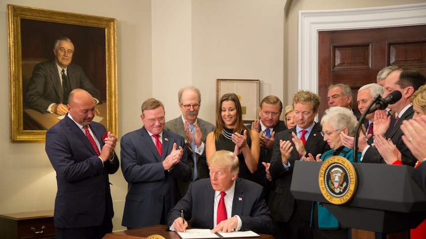 President Trump signs an executive order in the White House flanked by Vice President Pence and cabinet ministers.