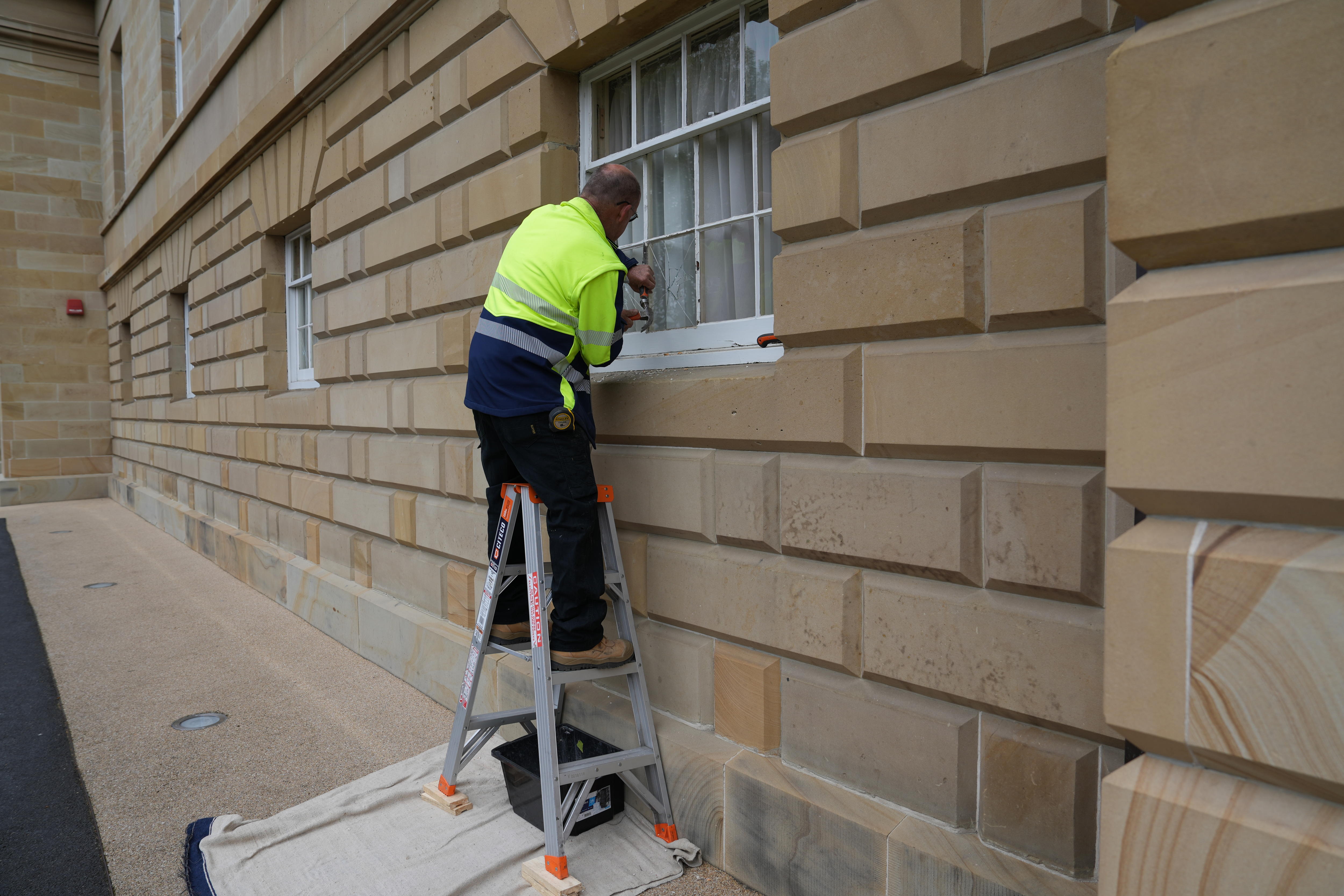 A man in high vis repairing broken windows on a sandstone building