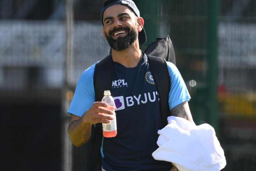 An Indian man laughs while holding a water bottle. 