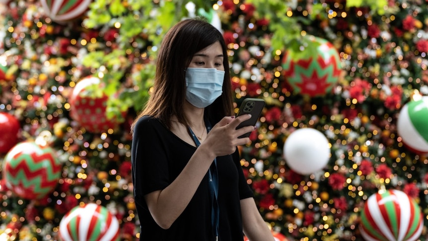 A woman wearing a protective face mask walking past the Martin Place Christmas Tree, Sydney, Friday, December 18, 2020. Prime Minister Scott Morrison has urged Australians to remain calm as a NSW virus cluster prompts some domestic borders to shutter close to Christmas. (AAP Image/James Gourley) NO ARCHIVING