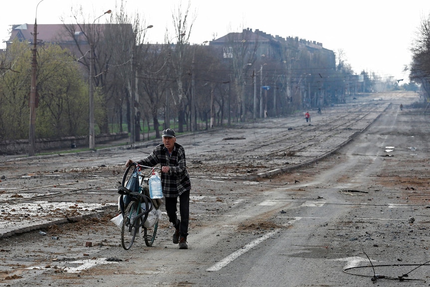 A man cycles his bicycle down a rubble-lined street.