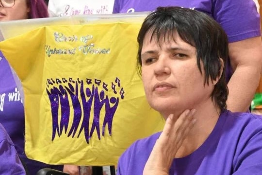 Danielle Alvers next to a banner with the words "the choir of unheard voices" visible on it 