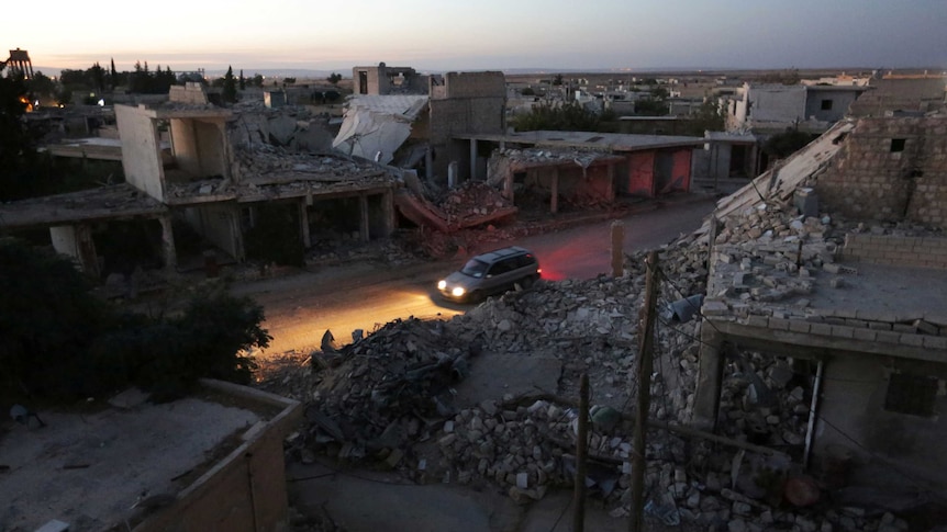 A vehicle drives past damaged buildings in the northern Syrian rebel-controlled town of al-Rai.