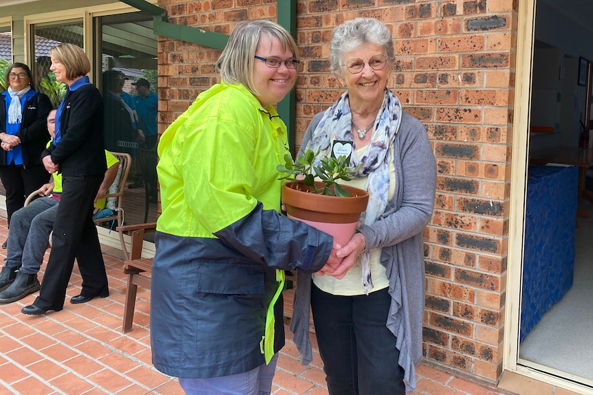 A woman hands another woman a pot plant