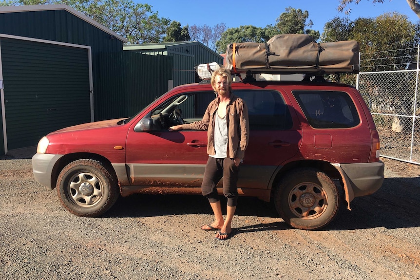 Mattis Mamczek stands next to his red four-wheel-drive, which has no windows and is covered in mud.